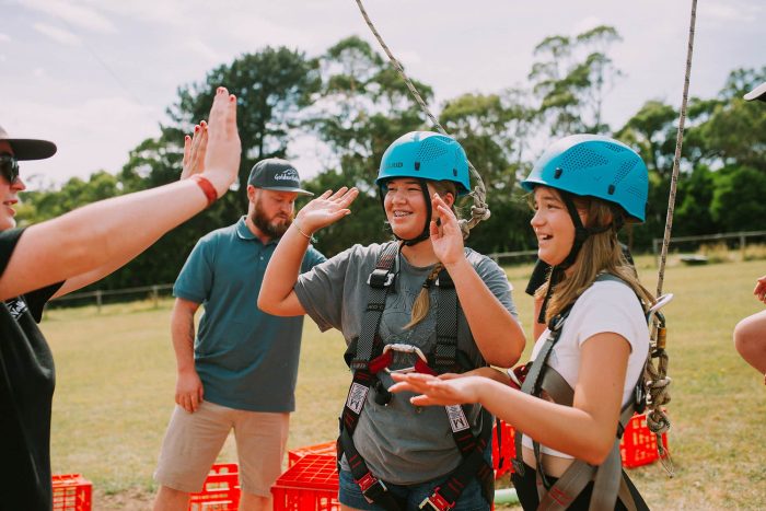 two girls at holiday camp in Melbourne wearing helmets and giving high fives after completing adventure activities.