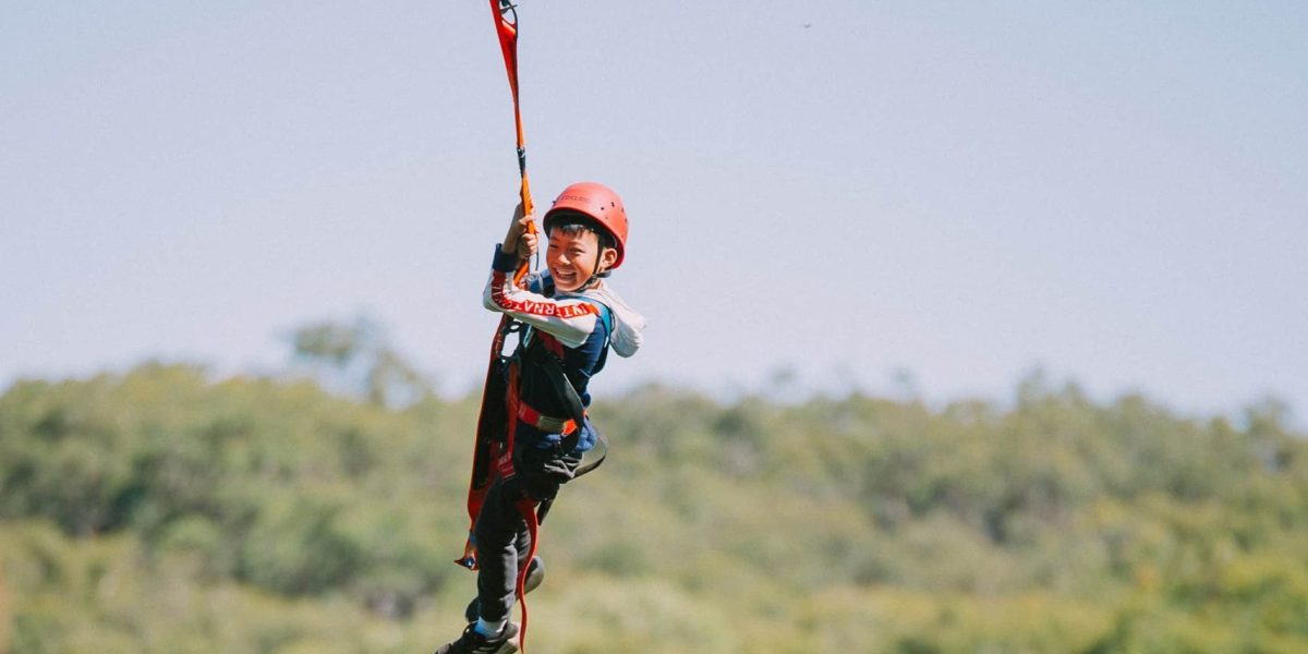Young boy on giant swing, swinging over tree tops of the valley.