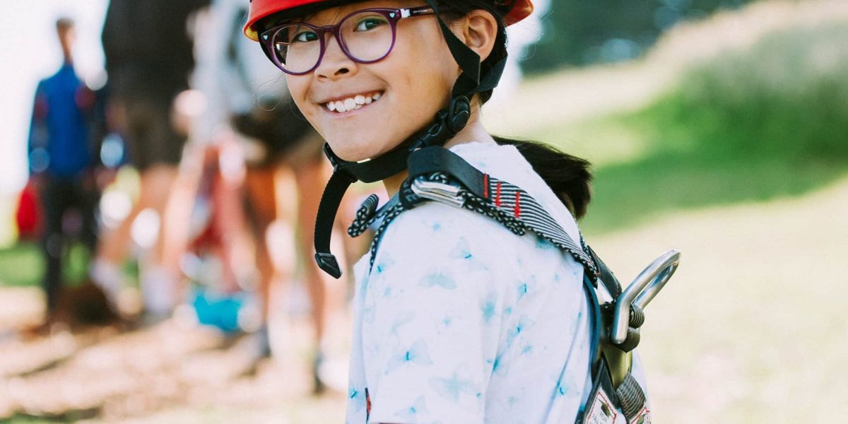 Young boy wearing helmet and harness, finished flying fox activity at Golden Valleys in Victoria, starring back to the camera with friends in the background