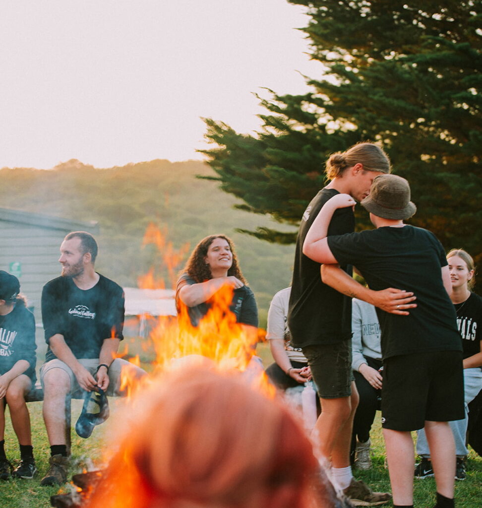 image of people gathered around a camp fire hugging at a training event.