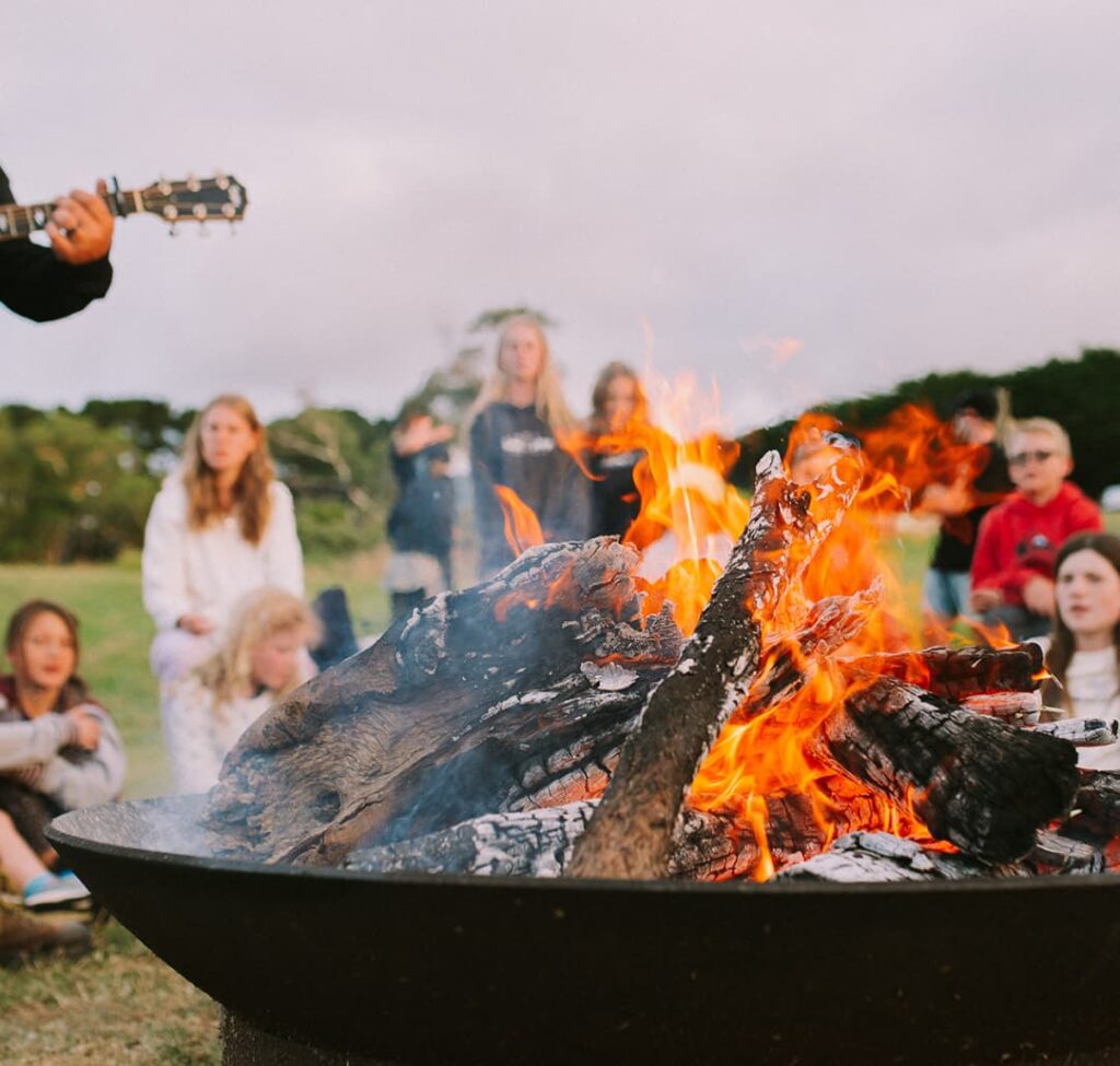 Picture of a church group sitting around the camp fire at church camp playing guitar.