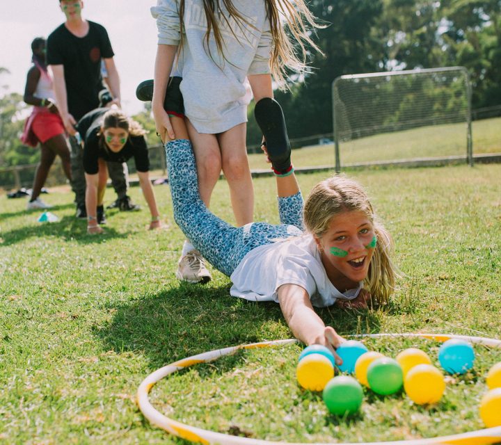 Girl reaching for coloured ball, playing soccer field team challenge games at her school camp in Victoria